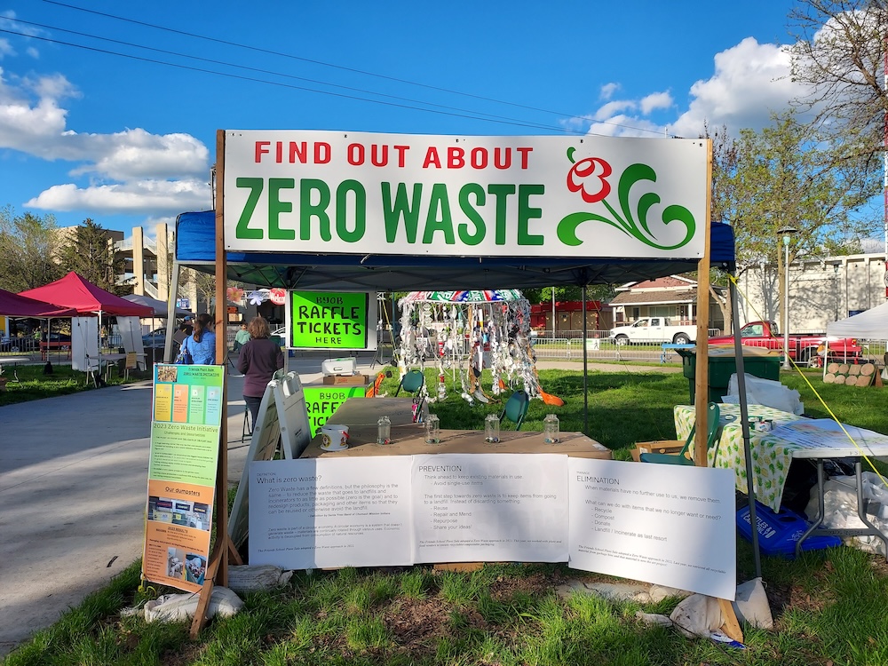 Photo of the Zero Waste Tent in the Garden Fair. There are informational signs about reducing waste, raffle ticket signs, and a large sculpture of a jellyfish made out of recycled items from the previous year's plant sale.